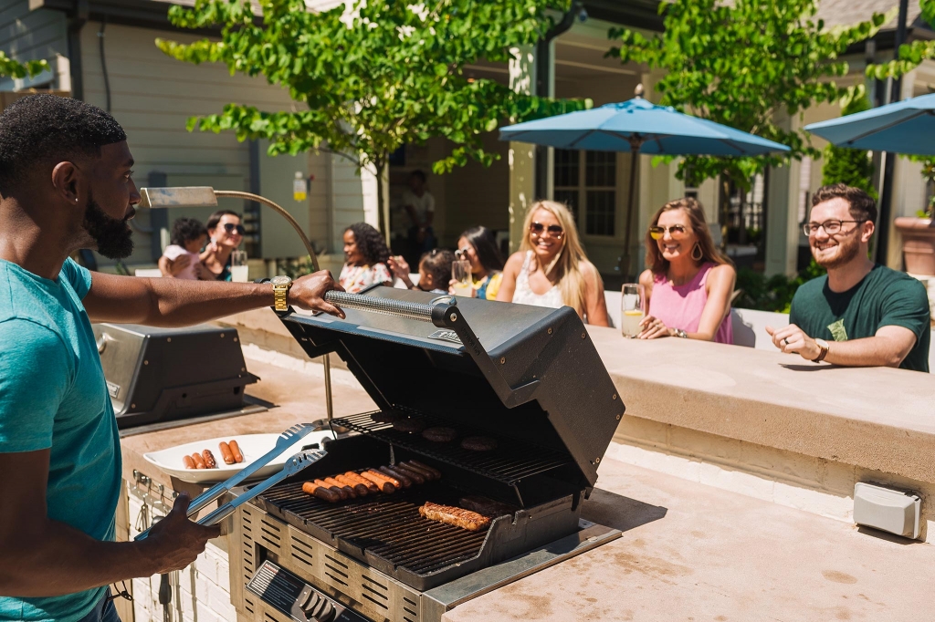 image of residents enjoying community amenities outside such as a barbecue grill and shade umbrellas 